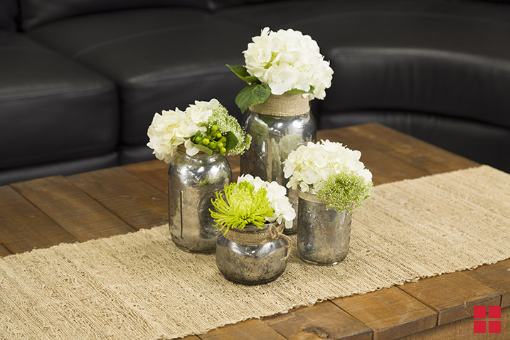 Four silver vases with white flowers and greenery in them. 