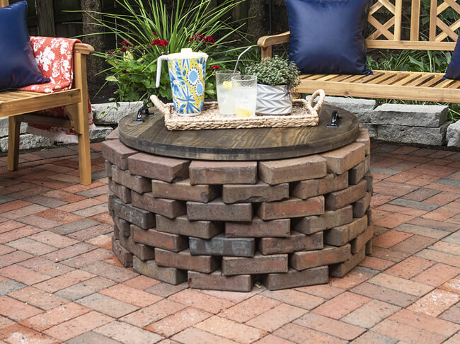 Clean patio with brick fire pit and stained wood fire pit cover with decorative tray and benches